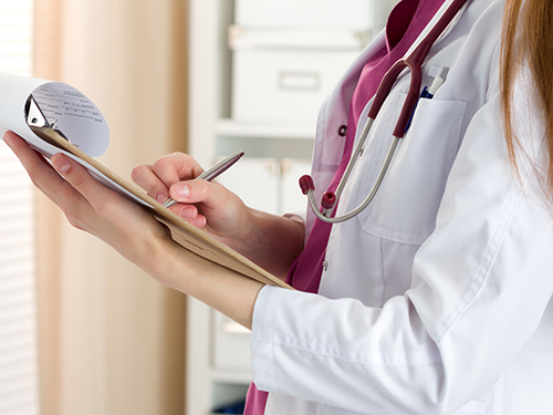 Close up view of female doctor hands holding clipping pad and filling patient history or prescribing some medicines. Healthcare and medical concept.